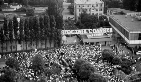 Tłum ludzi stojących pod bramą stoczni. Widoczny duży napis "Stocznia Gdańska im. Lenina"